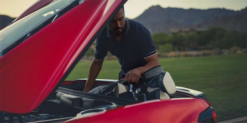 Man putting golf clubs in the trunk of a Corvette Stingray
