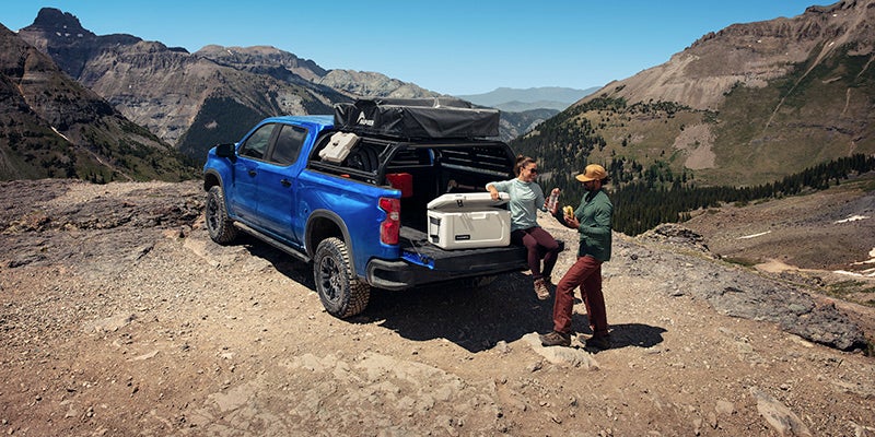Blue Chevrolet Silverado 1500 parked on a ledge of a mountain while two people have lunch outside