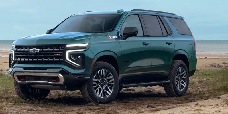 Blue Chevrolet Suburban parked on a beach next to an ocean while it is cloudy outside