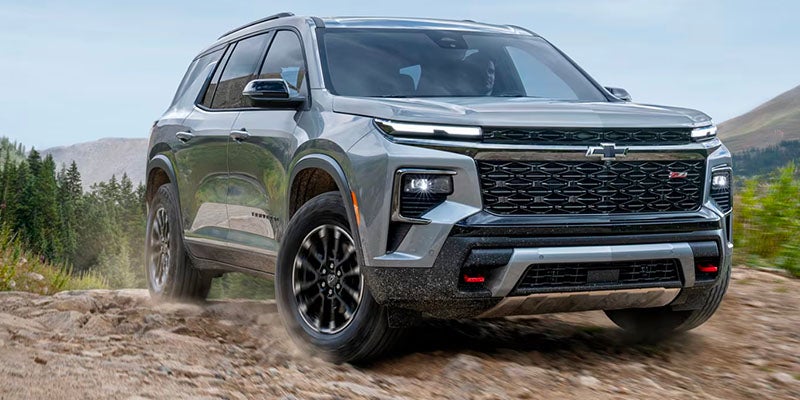 Gray Chevrolet Traverse going up hill outside by the forest