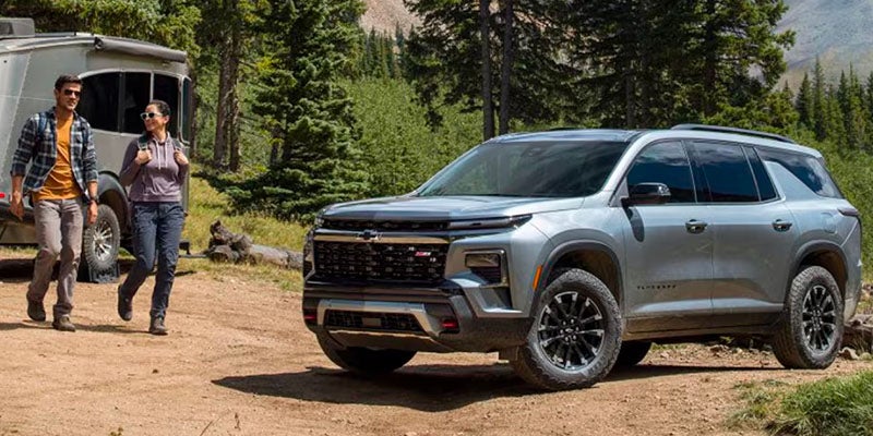 Gray Chevrolet Traverse parked on camp grounds as two people walk by smiling